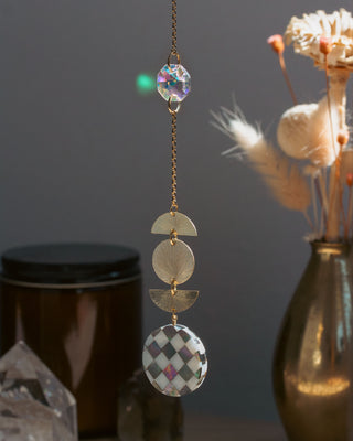 Decorative hanging ornament with geometric shapes and crystals against a dark background