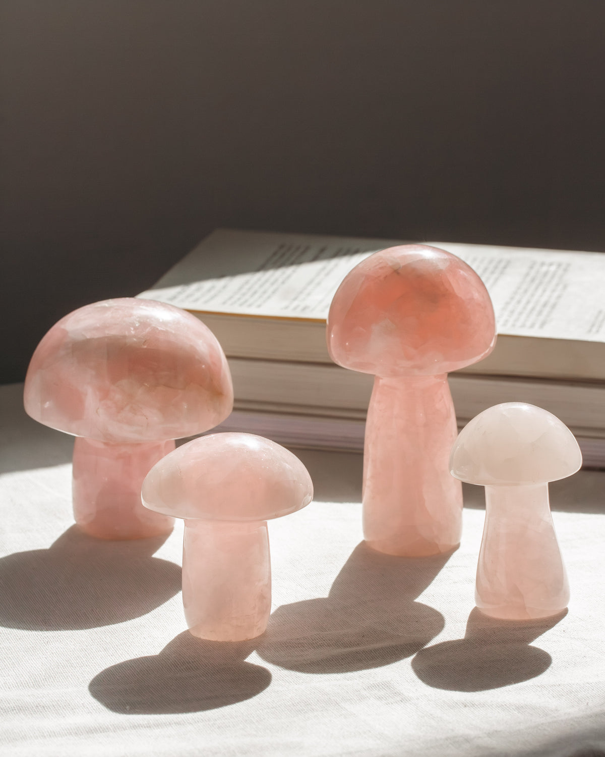 Four pink rose quartz crystal mushrooms on a dark surface with a book in the background