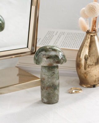 Decorative green stone mushroom sculpture on a white surface with a gold vase and framed artwork in the background.