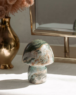Ocean Jasper patterned mushroom sculpture on a surface with a gold vase and mirror in the background.