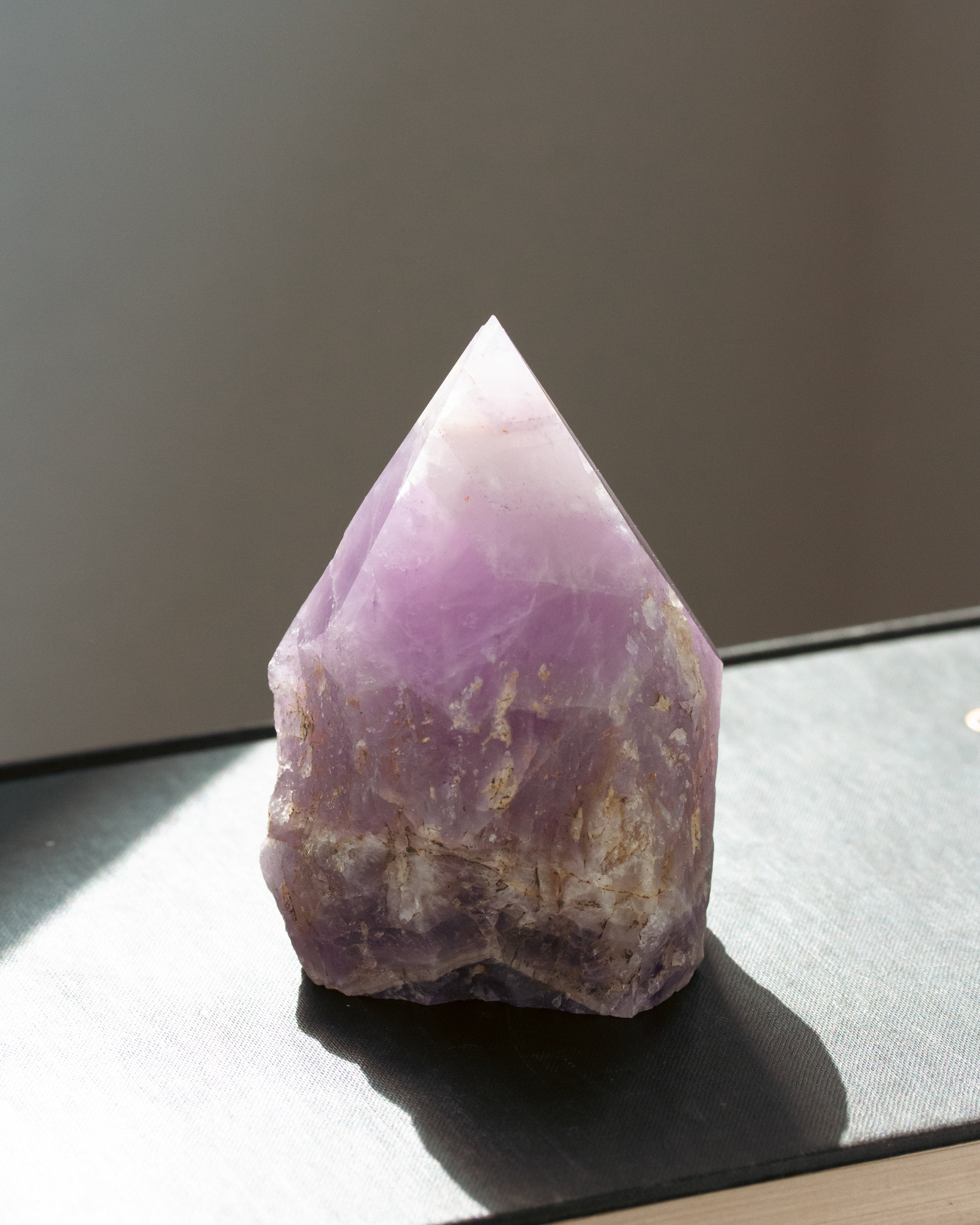 Purple amethyst gemstone crystal on a reflective surface with a neutral background
