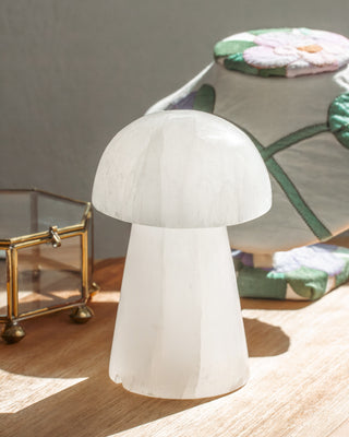 Mushroom-shaped candle lights up a selenite figurine on a wooden desk