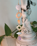 Decorative hanging with beads and stones on a white statue with green leaves in the background