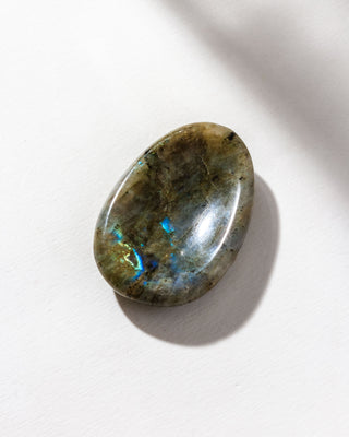 A smooth labradorite stone with a slight indent, placed on a white surface.