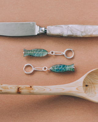 Knife with decorative handle, wooden spoon, and fish-shaped labradorite earrings on a brown surface
