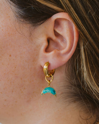 Woman wearing turquoise crescent moon charm gold hoop earring.
