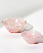 Two rose quartz nesting bowls on a neutral background, with a subtle wavy pattern.