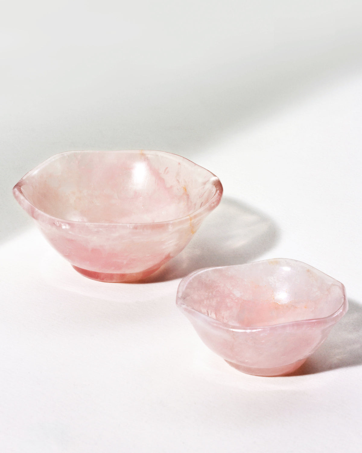 Two rose quartz nesting bowls on a neutral background, with a subtle wavy pattern.