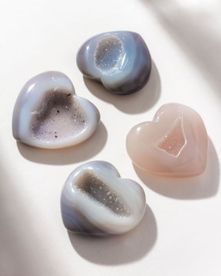 A collection of heart-shaped druzy agate stones with a smooth surface and sparkling crystal layers within, displayed on a light background.
