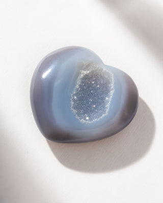 Blue colored heart shaped druzy agate curio on a white surface.