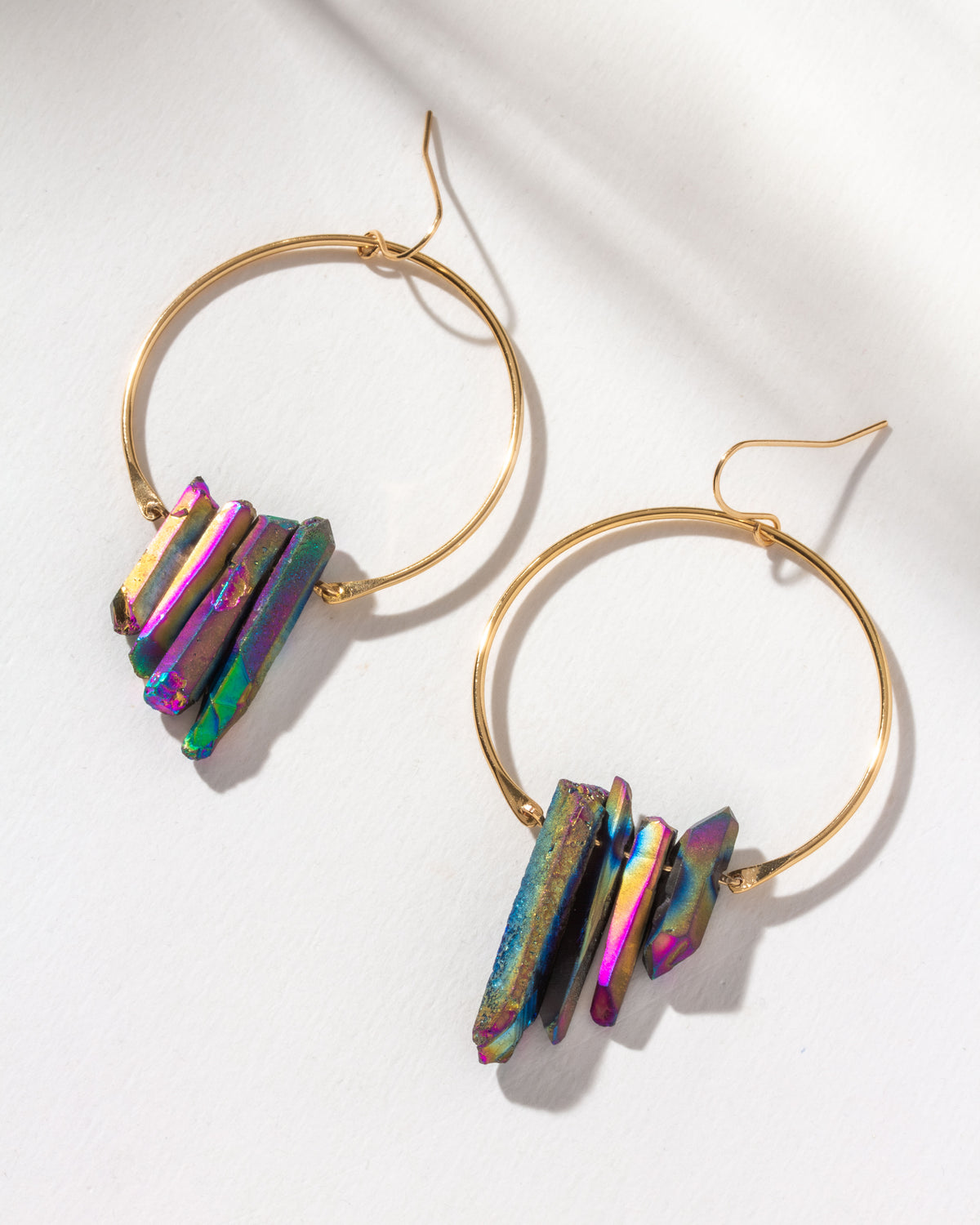 Pair of gold hoop earrings with multicolored metallic purple quartz crystals attached to the hoops.