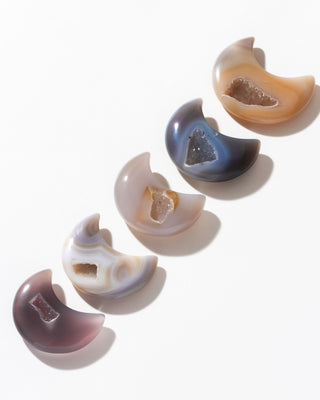 Various druzy agate gemstone crescent moon curios arranged in a row against a white background.