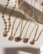 Several gold chain necklaces with neutral-toned gemstones are displayed against a white background.
