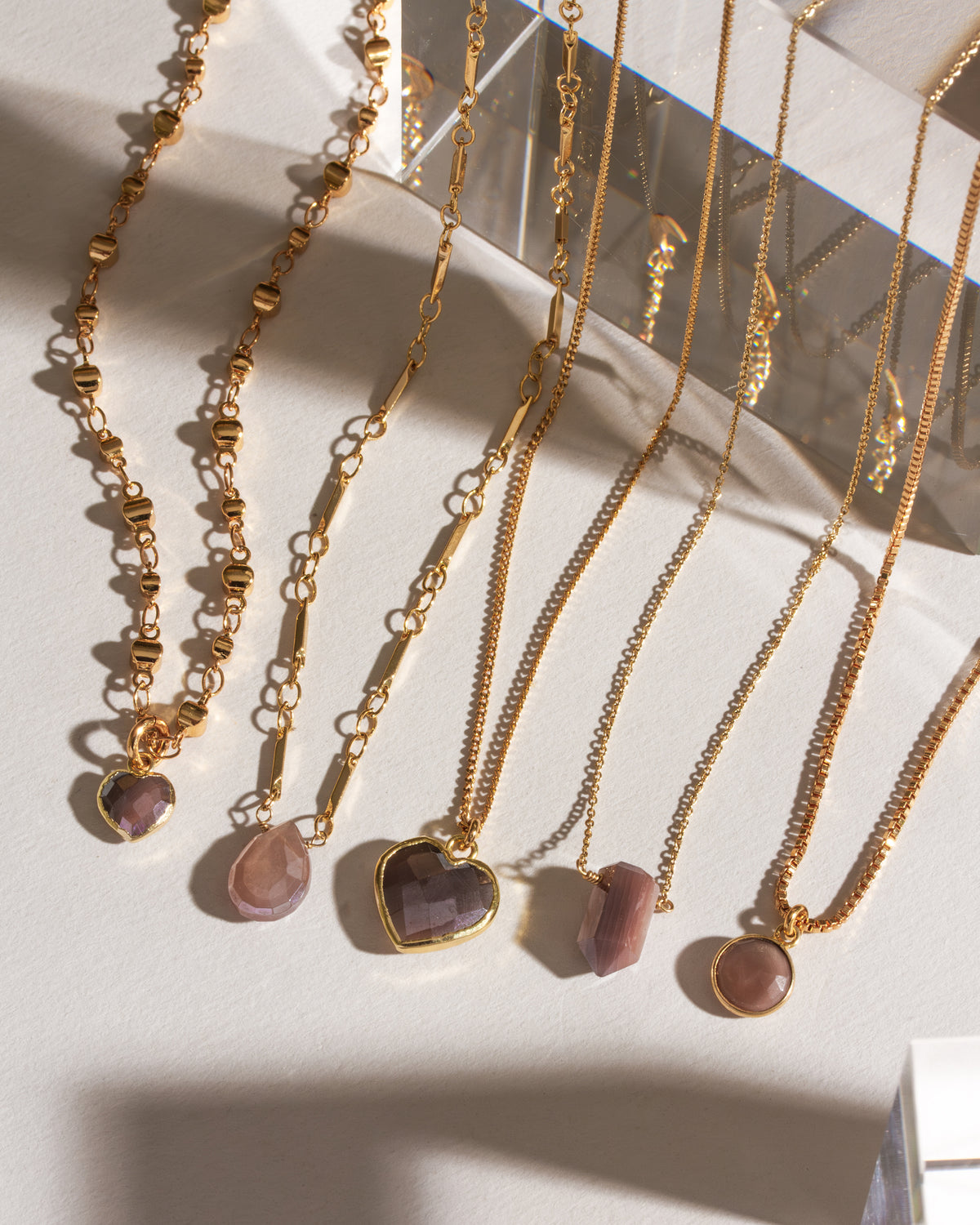 Several gold chain necklaces with neutral-toned gemstones are displayed against a white background.