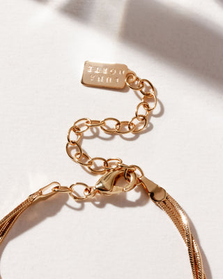 Detail of necklace lobster clasp with chain extender and Luna Norte gold brand tab, on a white surface.