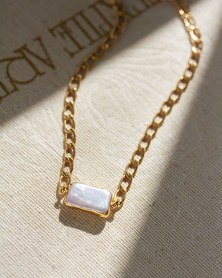 Sleek, modern, minimalist collar chain necklace with a uniquely geometric rectangular pearl on a textured fabric surface.