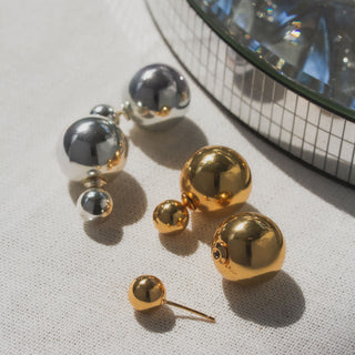 Pair of gold and silver spherical earrings on a textured surface.