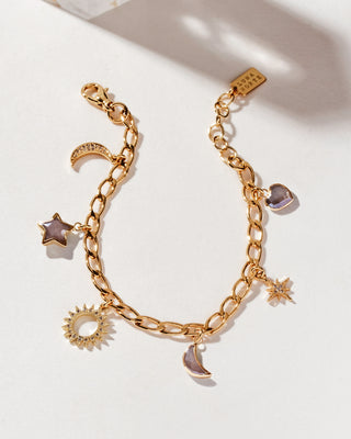 A gold-tone charm bracelet with various celestial charms including a coffee moonstone crescent moon, a star, and a sunburst, displayed against a neutral background.