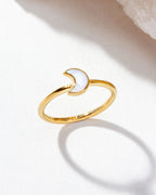 Gold ring with moonstone shaped as a crescent moon displayed on a tabletop.