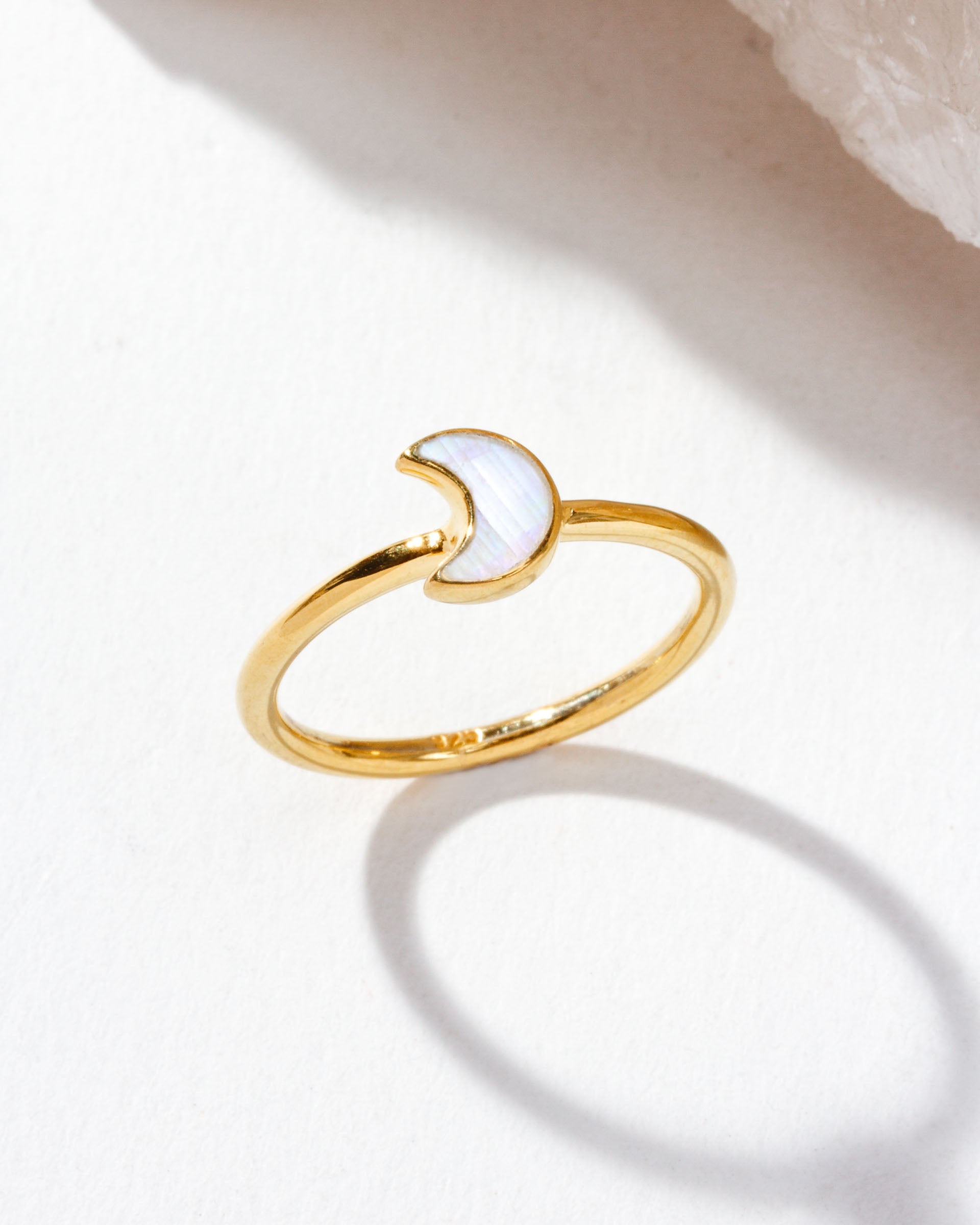 Gold ring with moonstone shaped as a crescent moon displayed on a tabletop.