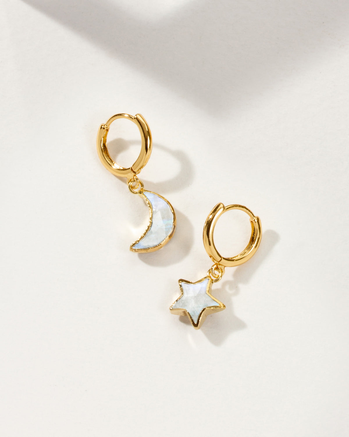 Pair of mismatched gold huggie hoop earrings with moonstone star and moon charms