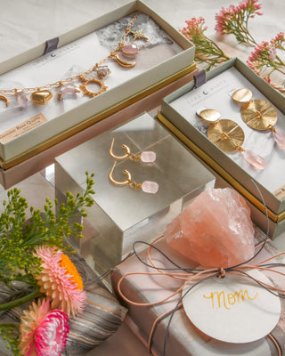 Jewelry set with gold earrings and necklaces in open boxes, surrounded by flowers.