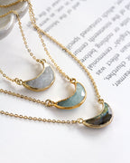Three necklaces with semi-circular gemstone pendants on a white surface