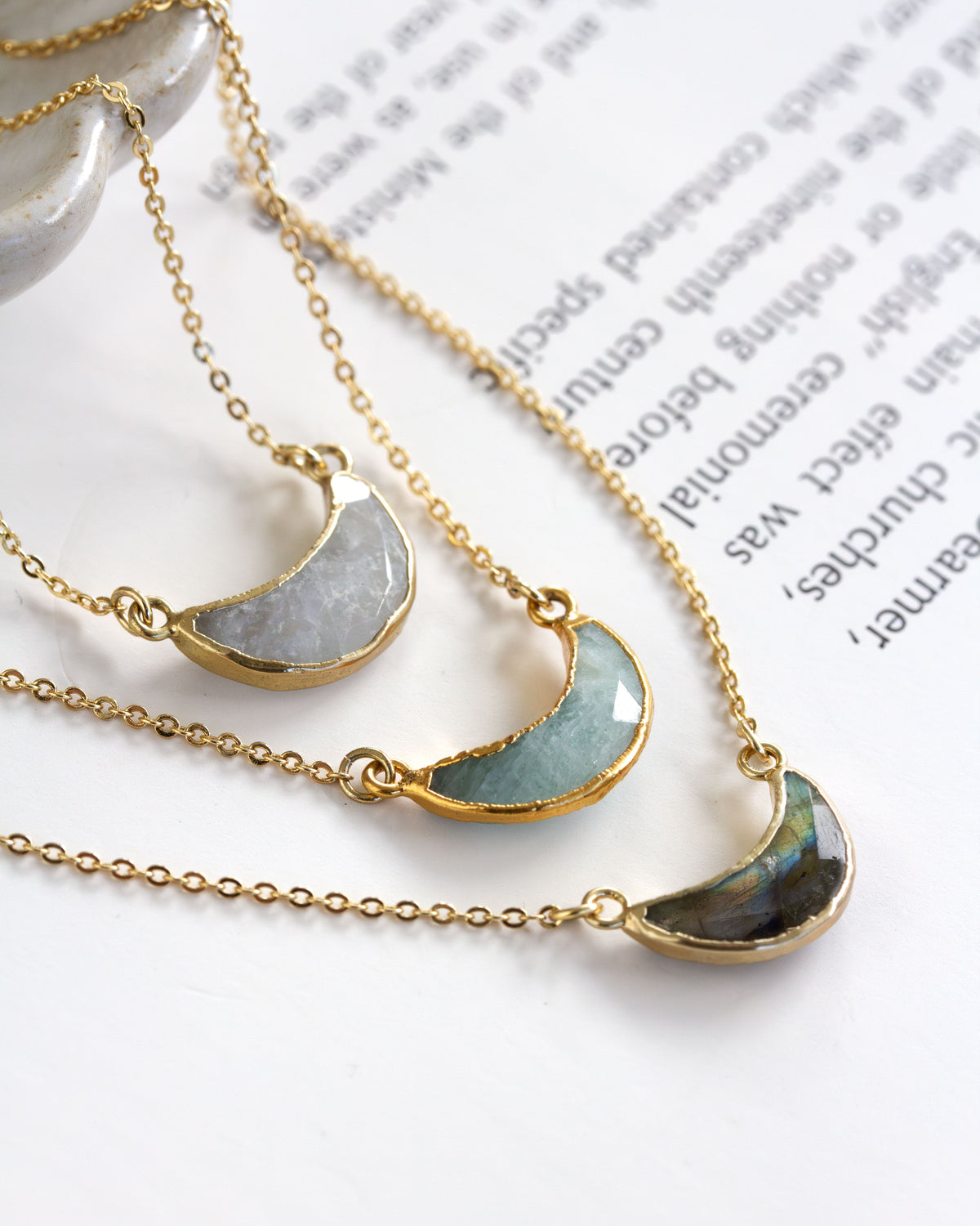 Three necklaces with semi-circular gemstone pendants on a white surface