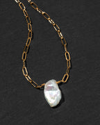 A gold paperclip chain necklace with a  white Keshi pearl pendant.