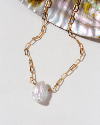 Gold chain necklace with a pearl pendant on a white background