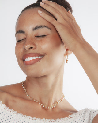 Woman wearing a delicate beaded pearl necklace with multi-color accents and gold initial letter earrings 