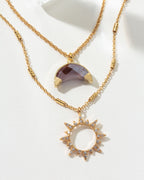 Gold necklace set with a moonstone pendant and a sunburst pendant with gems.