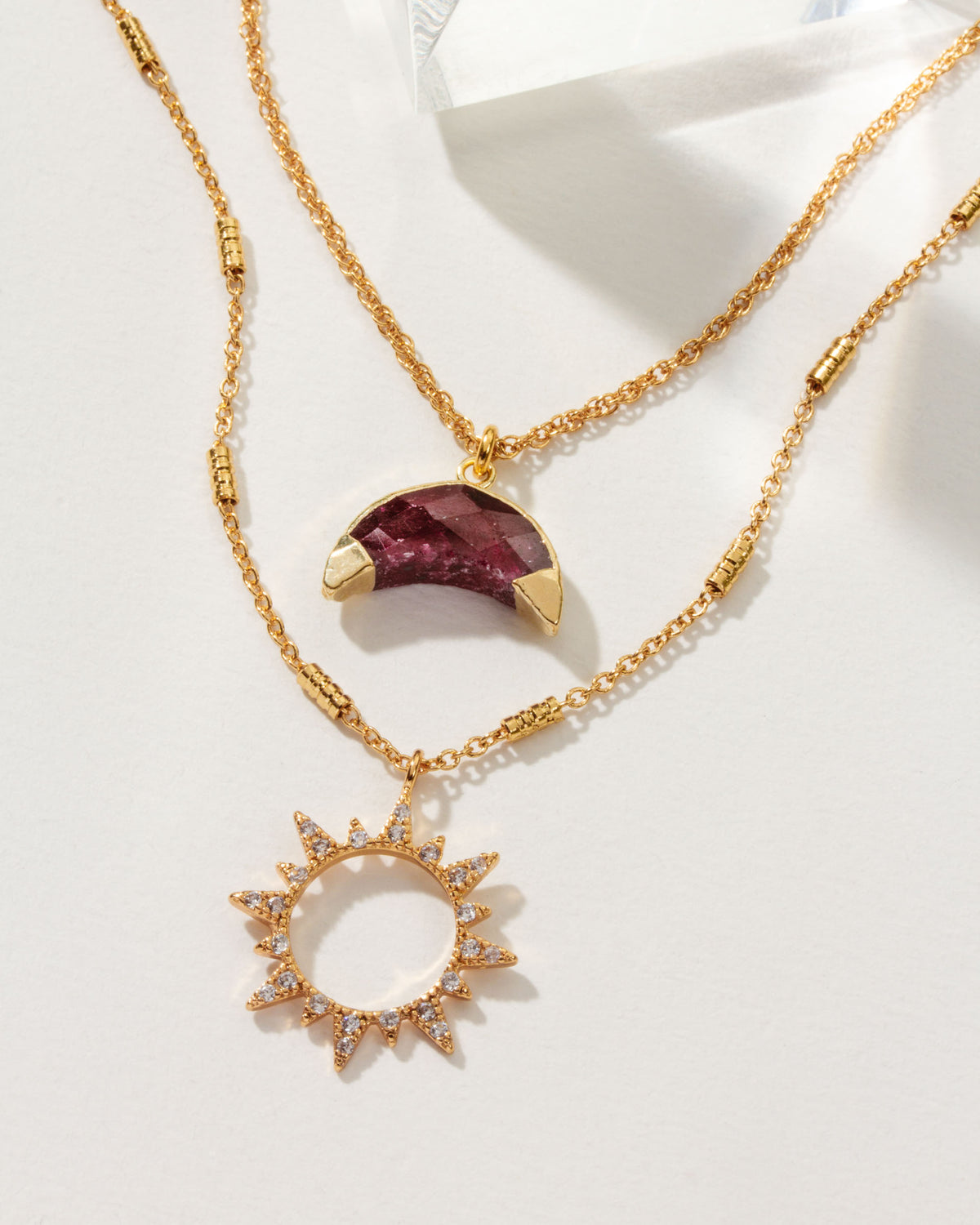 Gold necklace set with a ruby crescent moon and a sunburst pendant with crystal accents.