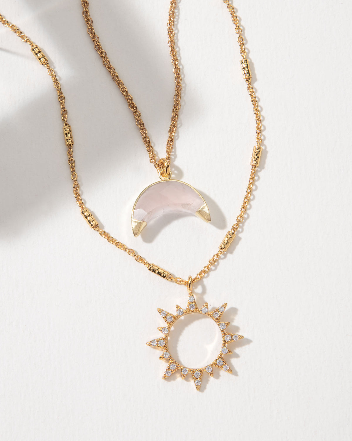 Gold necklace set with a sun pendant and a rose quartz moon pendant.