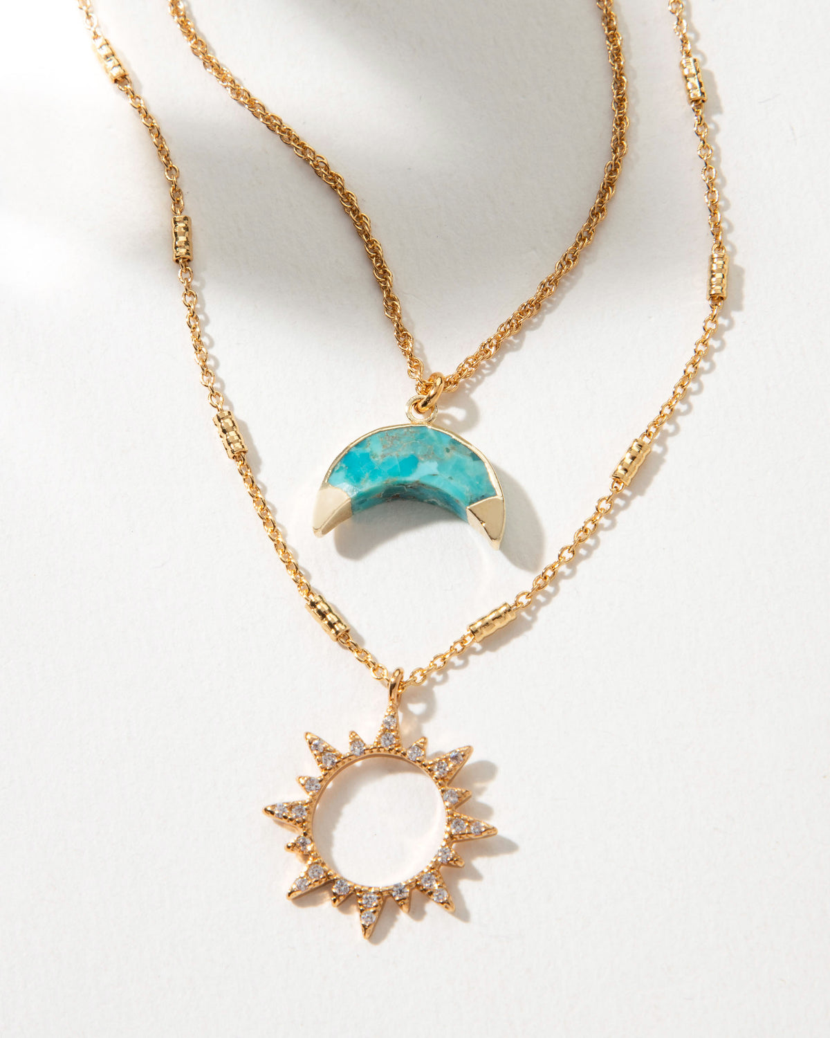 Gold necklace set with a turquoise crescent moon and sunburst pendant.