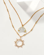 Gold necklace set with a moonstone crescent and a sunburst pendant with small stones.