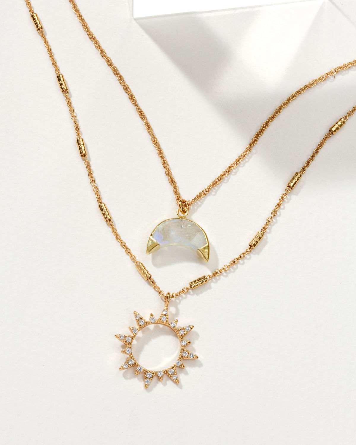 Gold necklace set with a moonstone crescent and a sunburst pendant with small stones.