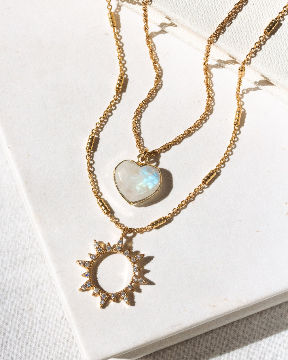 Two gold layering necklaces, one with moonstone heart and other with CZ sun pendants