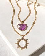 Gold necklace with amehtyst heart and sun pendant on a white background