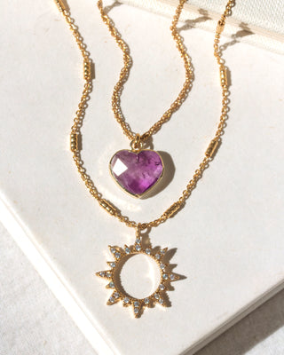 Gold necklace with heart and sun pendant on a white background