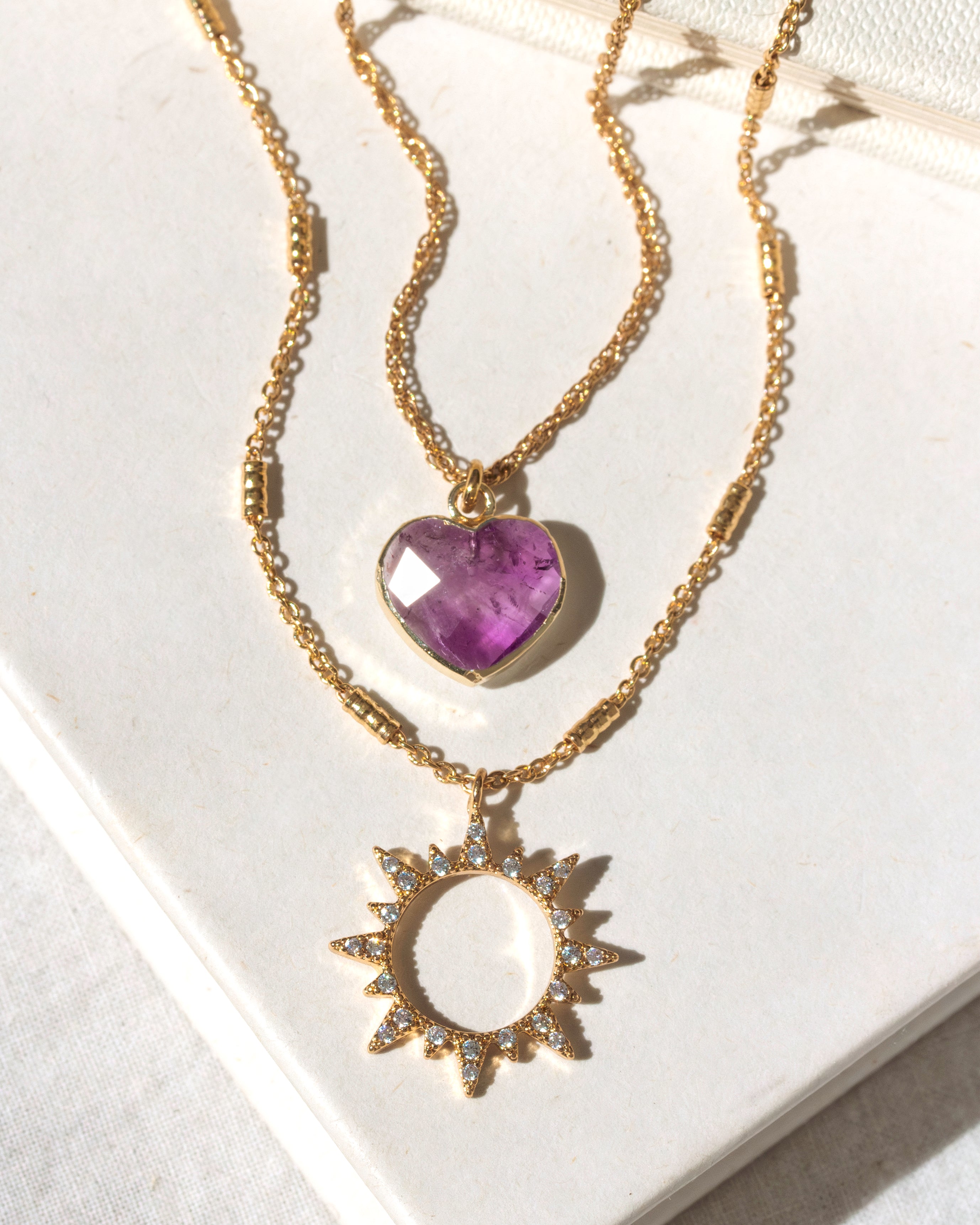 Gold necklace with amehtyst heart and sun pendant on a white background