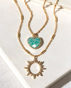 Two gold necklaces with amazonite heart and sun pendants on a white surface
