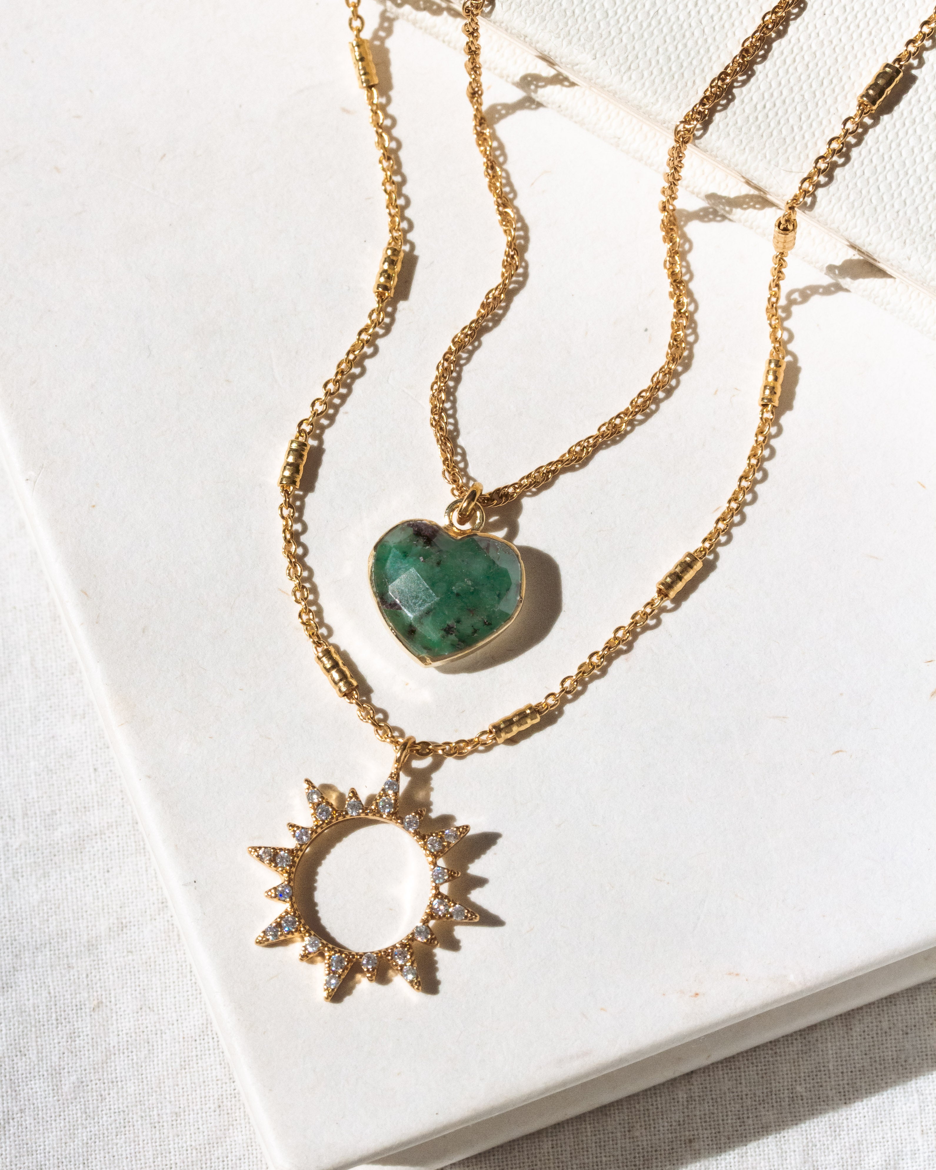 Two gold necklaces with emerald heart and sun-shaped pendants