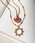 Gold necklaces with strawberry quartz heart and sun-shaped pendants on a white background