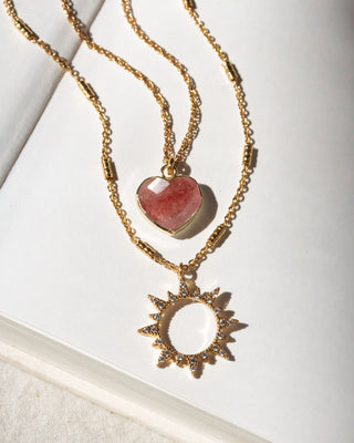Gold necklaces with heart and sun-shaped pendants on a white background