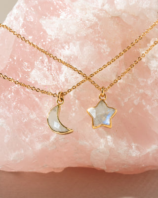 Two delicate gold chain necklaces with moon and star-shaped pendants resting on a pink crystal. 