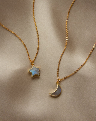 Two delicate gold chain necklaces with small pendants, one star-shaped and one crescent moon-shaped, both featuring iridescent moonstone stones.