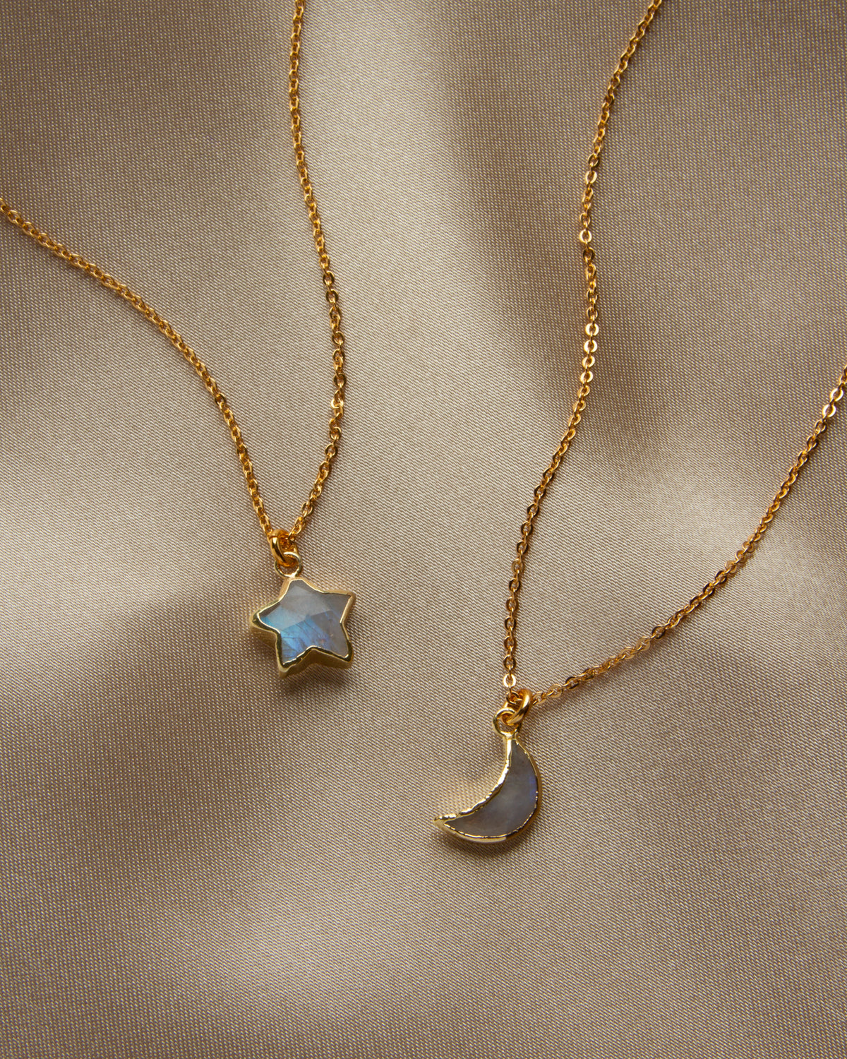 Two delicate gold chain necklaces with small pendants, one star-shaped and one crescent moon-shaped, both featuring iridescent moonstone stones.