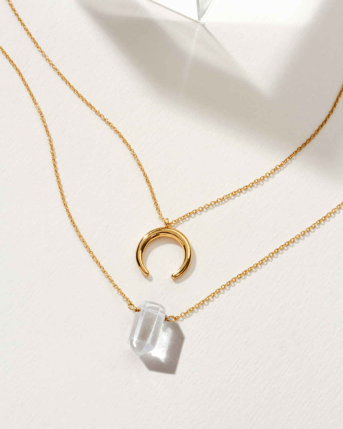 Gold necklaces featuring a crescent moon charm and a Clear Quartz point.