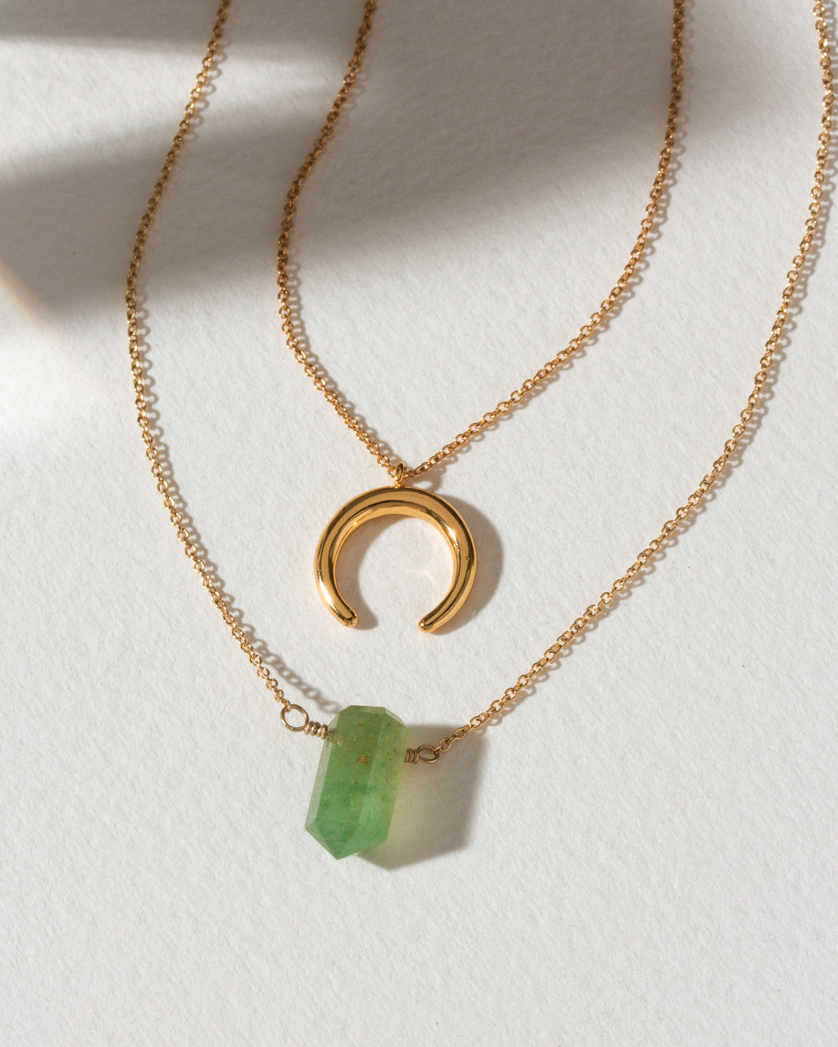Gold necklaces with a green aventurine point and crescent moon charm.
